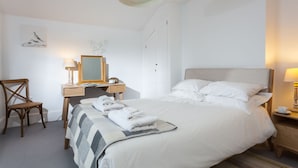A hotel room with a bed, a desk with a chair, a lamp, and a mirror.