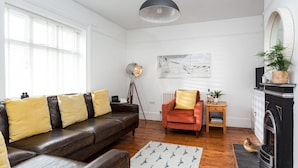 A living room with a leather sofa, a red armchair, a floor lamp, a fireplace, and a painting on the wall.
