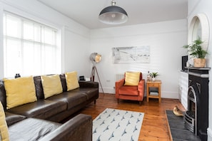 Een woonkamer met een leren bank, een rode fauteuil, een vloerlamp, een open haard en een schilderij aan de muur.