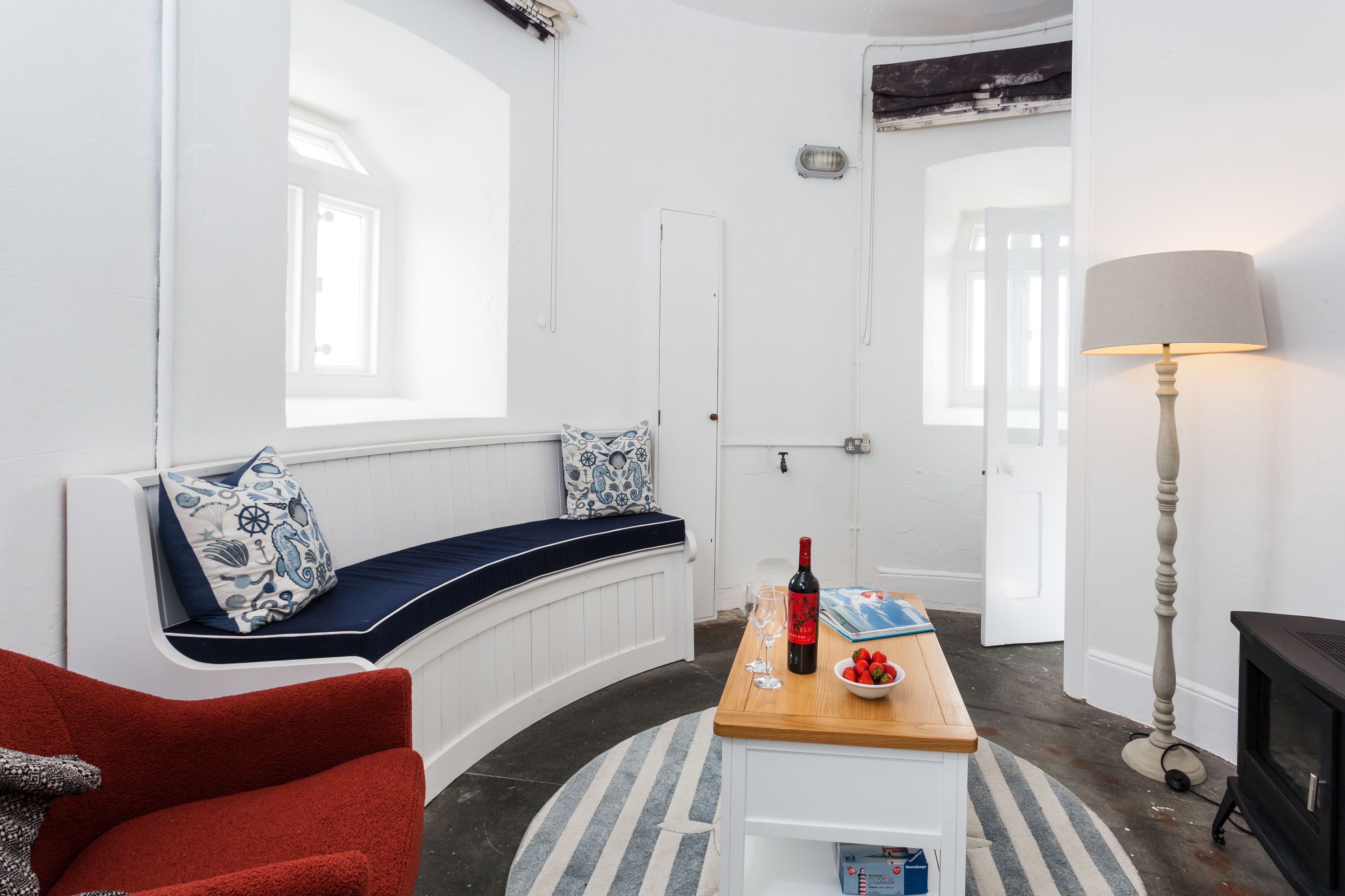 Una habitación con un banco curvo, una mesa de madera con una botella y vasos, una lámpara y una chimenea.