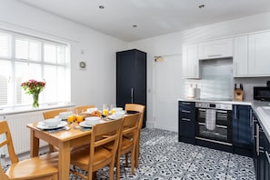 Een moderne keuken met een eethoek, met een zwart kastje, witte kasten, een patroon vloer en een raam met zonwering.