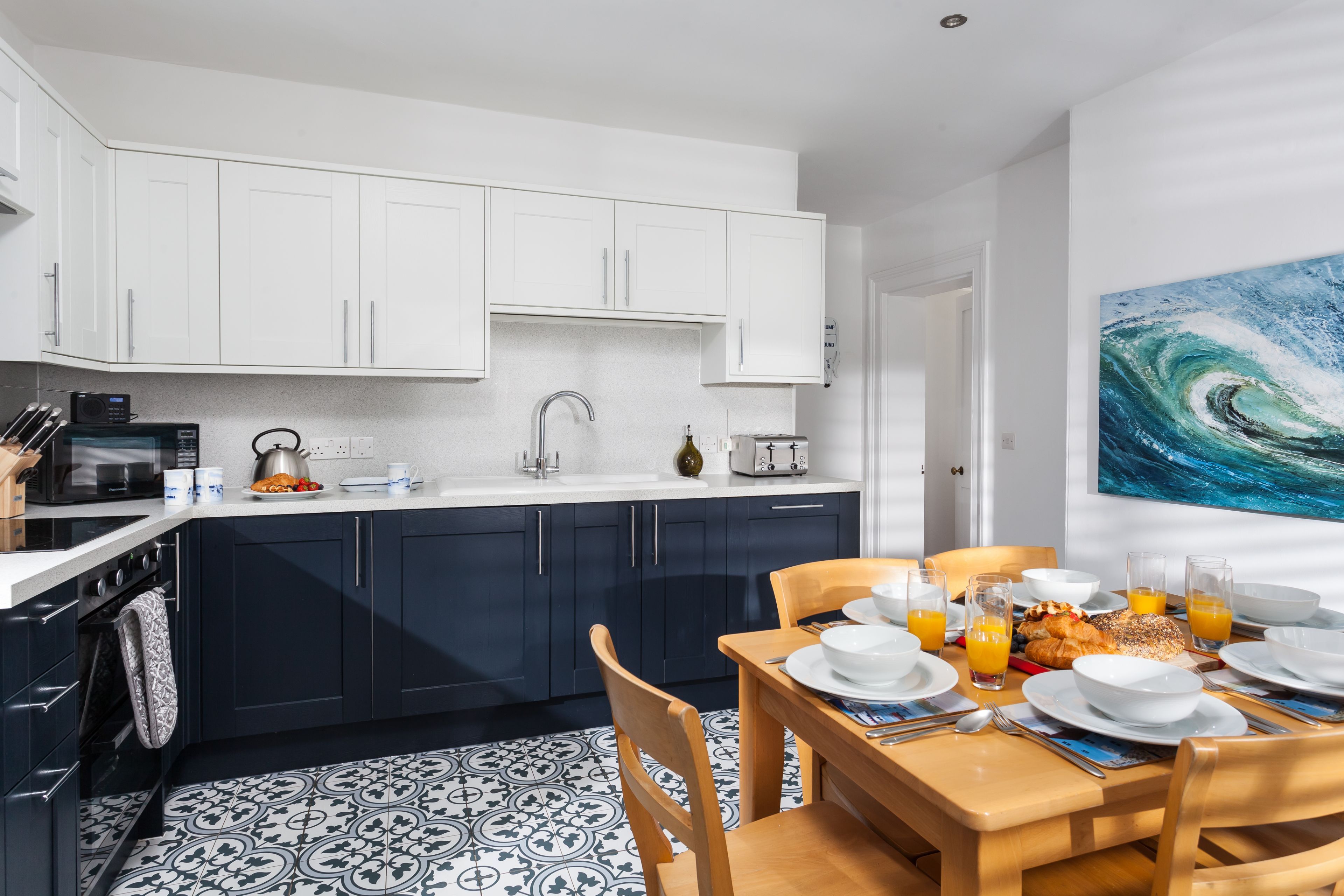 A modern kitchen with white cabinets, a black stove, and a dining area with a wooden table set for breakfast.