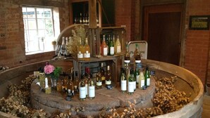 A wine cellar with a circular stone structure filled with bottles and a wooden shelf with more bottles. - Luxury Coach House in beautiful rural village, scenic walks & 3 miles to Ledbury (Ledbury)