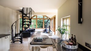 A spacious living area with a staircase, a dining table, and a large window providing a view of the outdoors. - Luxury Coach House in beautiful rural village, scenic walks & 3 miles to Ledbury (Ledbury)