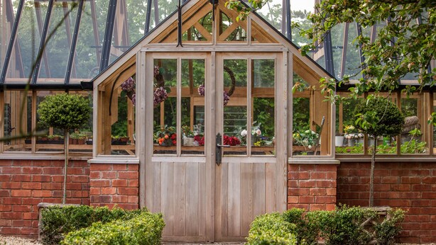 A greenhouse with a wooden door, large windows, and various plants. - Luxury Coach House in beautiful rural village, scenic walks & 3 miles to Ledbury (Ledbury)