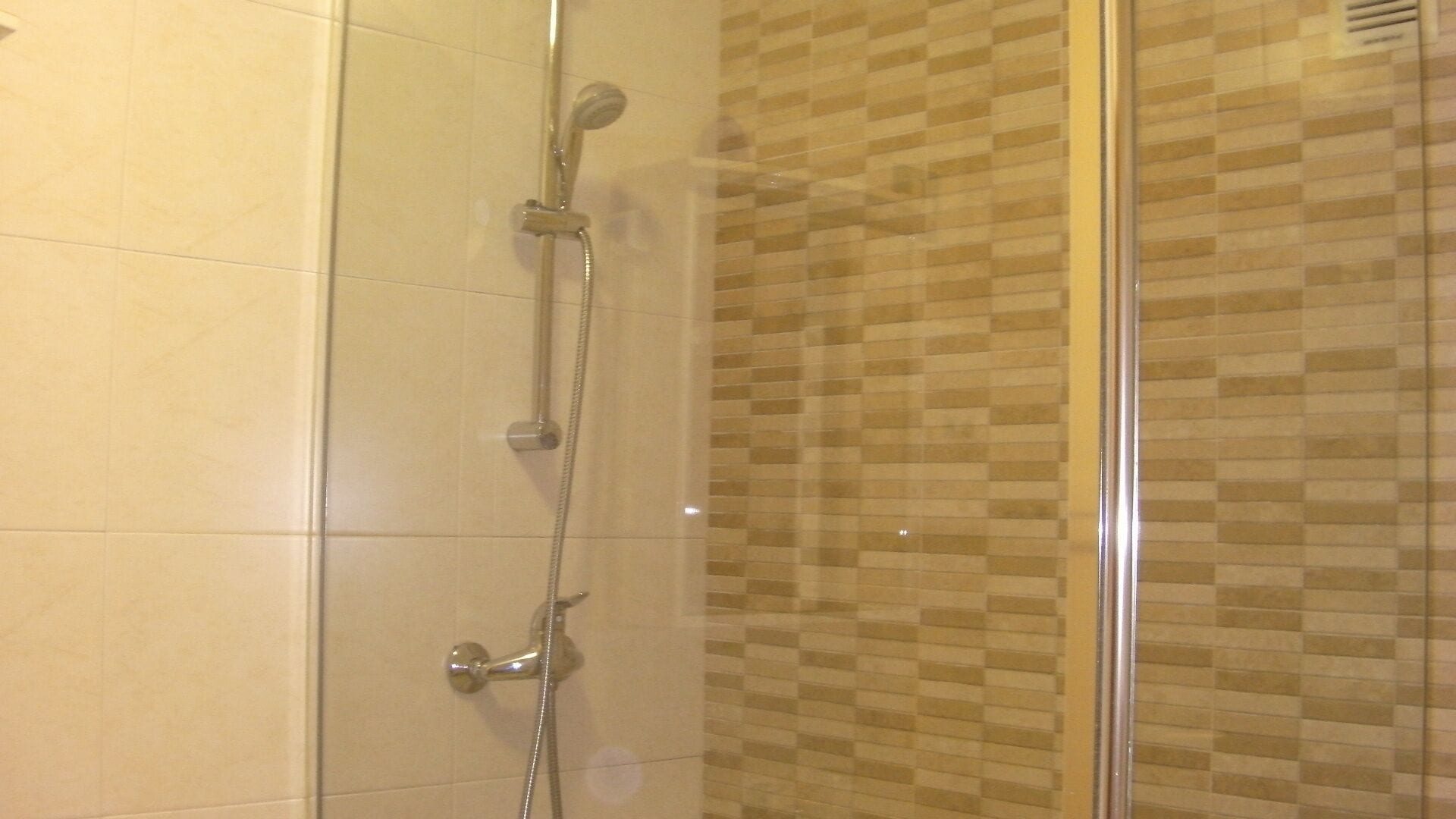 Eine Dusche mit Glastür und gefliesten Wänden.