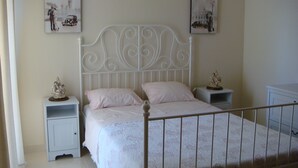 Ein Schlafzimmer mit weißem Metallbettgestell, zwei Nachttischen und zwei an der Wand hängenden Bildern.