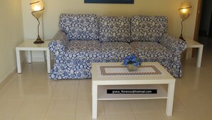 Ein Wohnzimmer mit einem gemusterten Sofa, zwei Beistelltischen, einem Couchtisch mit einer Vase und zwei Stehlampen.