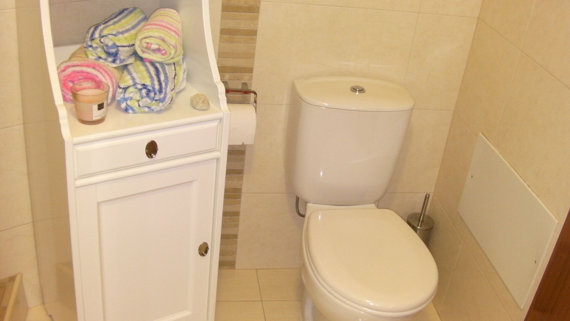 Une petite salle de bain comprenant des toilettes, un lavabo avec un miroir et une étagère avec des serviettes et un verre d’eau.