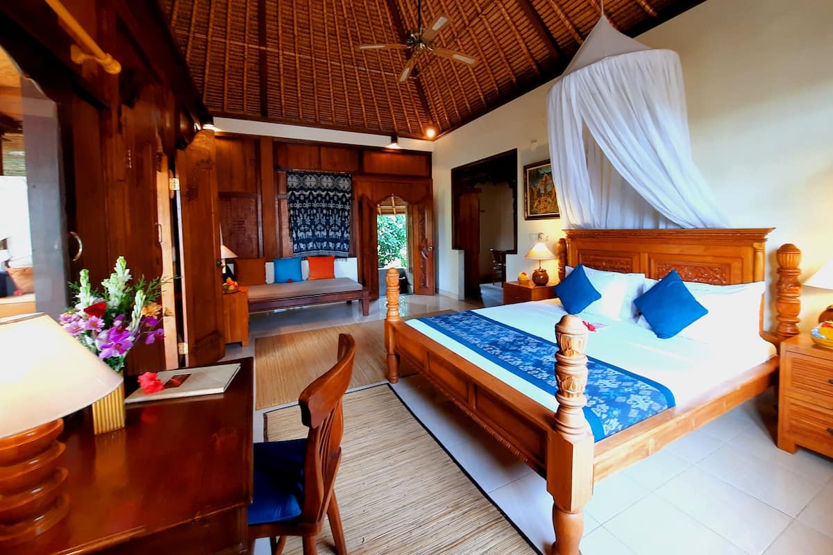 A room with a bed, a desk, a chair, a wooden bench, and a ceiling fan.