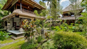 A traditional thatched-roof house with a balcony, surrounded by lush greenery and a small pond. - Alam Indah Ubud (Ubud)