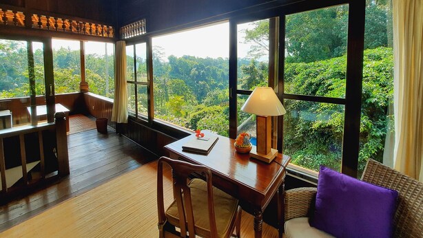 A room with large windows, a wooden desk, a chair, and a purple cushion. - Alam Indah Ubud (Ubud)