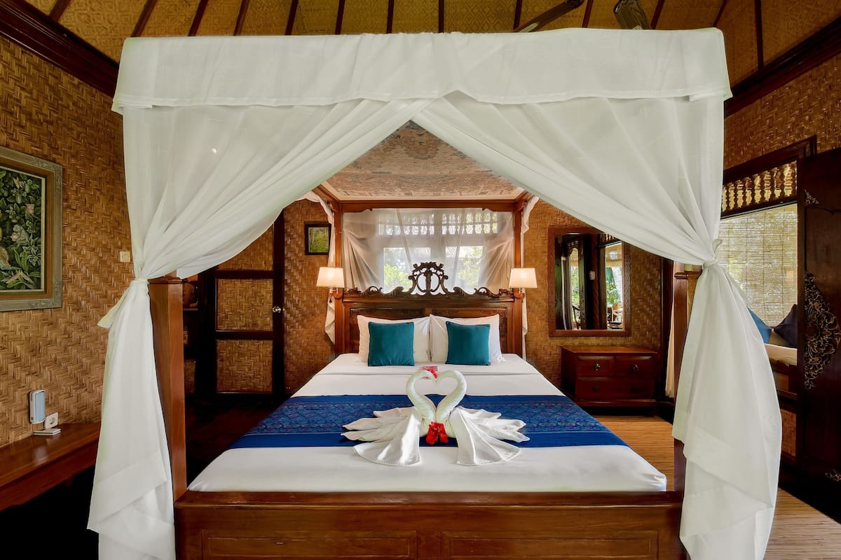 A hotel room with a bed under a canopy, a wooden headboard, and a blue bedspread.