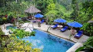 A pool area with lounge chairs and umbrellas, surrounded by lush greenery. - Alam Indah Ubud (Ubud)