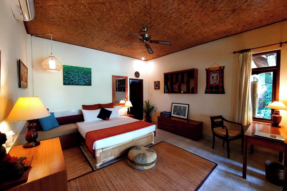 A cozy hotel room with a bed, bedside lamps, a wooden ceiling, a desk, and a chair.