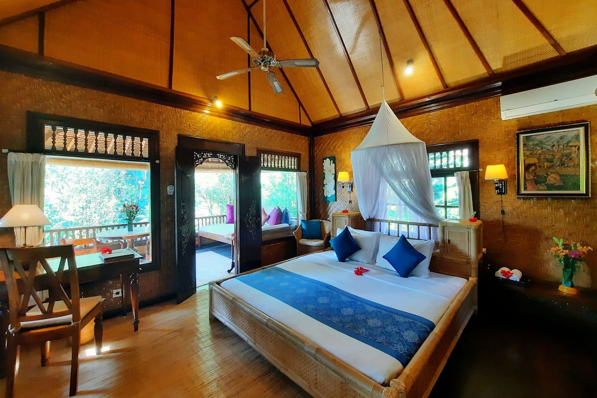 A spacious bedroom with a large bed, a ceiling fan, and a view of the outdoors through a window.