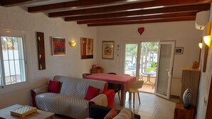 A cozy living room with a sofa, a small table, and a dining area with a table and chairs. There is a sliding glass door leading to an outdoor area.