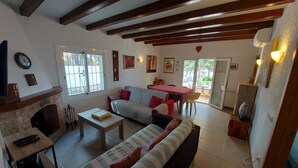 A living room with a sofa, a coffee table, and a fireplace. There is a dining area with a table and chairs.