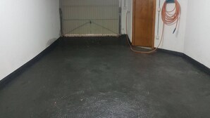 Een kamer met een betonnen vloer, een gesloten deur en een opgerolde kabel aan de muur.