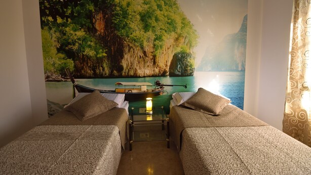 A room with two beds, a small table with a lamp, and a mural of a boat on water. - Villa Nirvan with Heated Pool (playa blanca, yaiza, lanzarote)