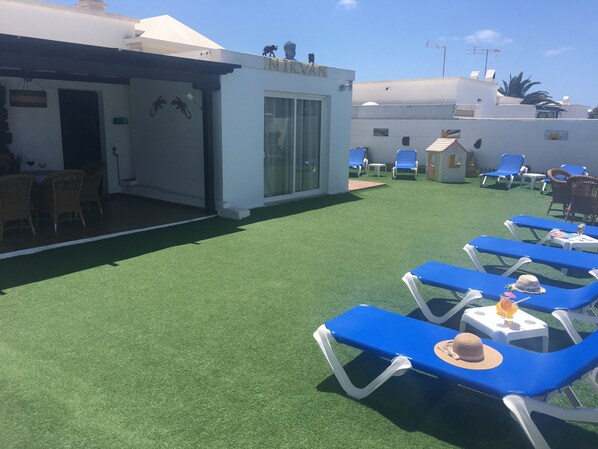 A rooftop terrace with artificial grass, blue lounge chairs, and a small seating area with wicker chairs. - Villa Nirvan with Heated Pool (playa blanca, yaiza, lanzarote)