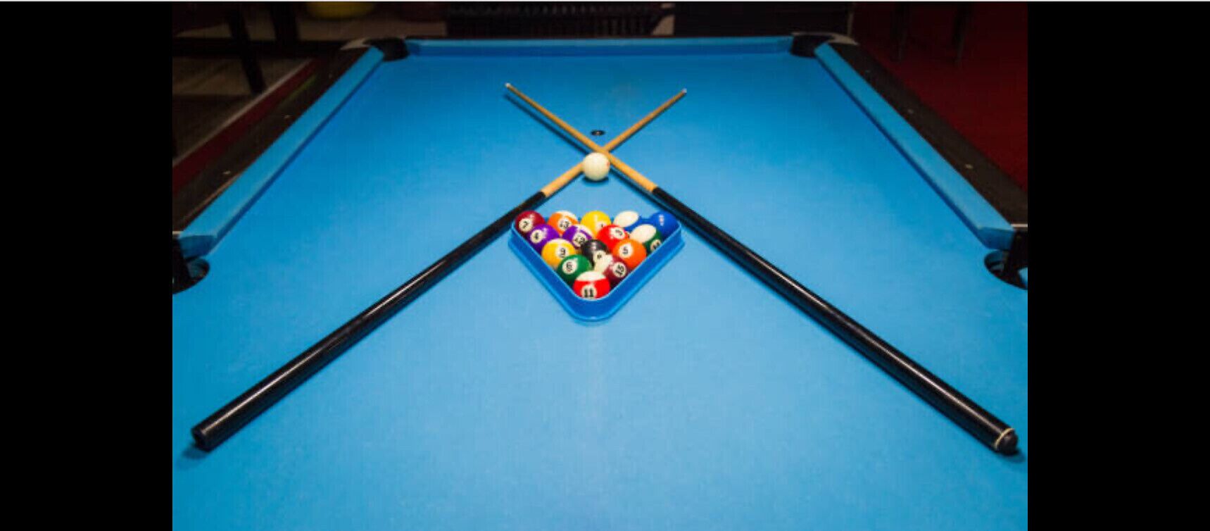 A pool table with a blue felt surface, a set of pool cues, and a rack of billiard balls.