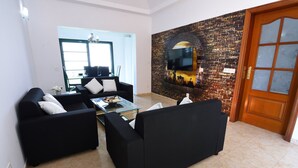 A living room with black sofas, a glass coffee table, and a brick wall with a TV. - Villa Nirvan with Heated Pool (playa blanca, yaiza, lanzarote)