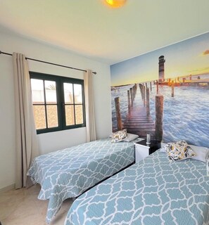 A room with two beds, a large window with curtains, and a mural of a pier.