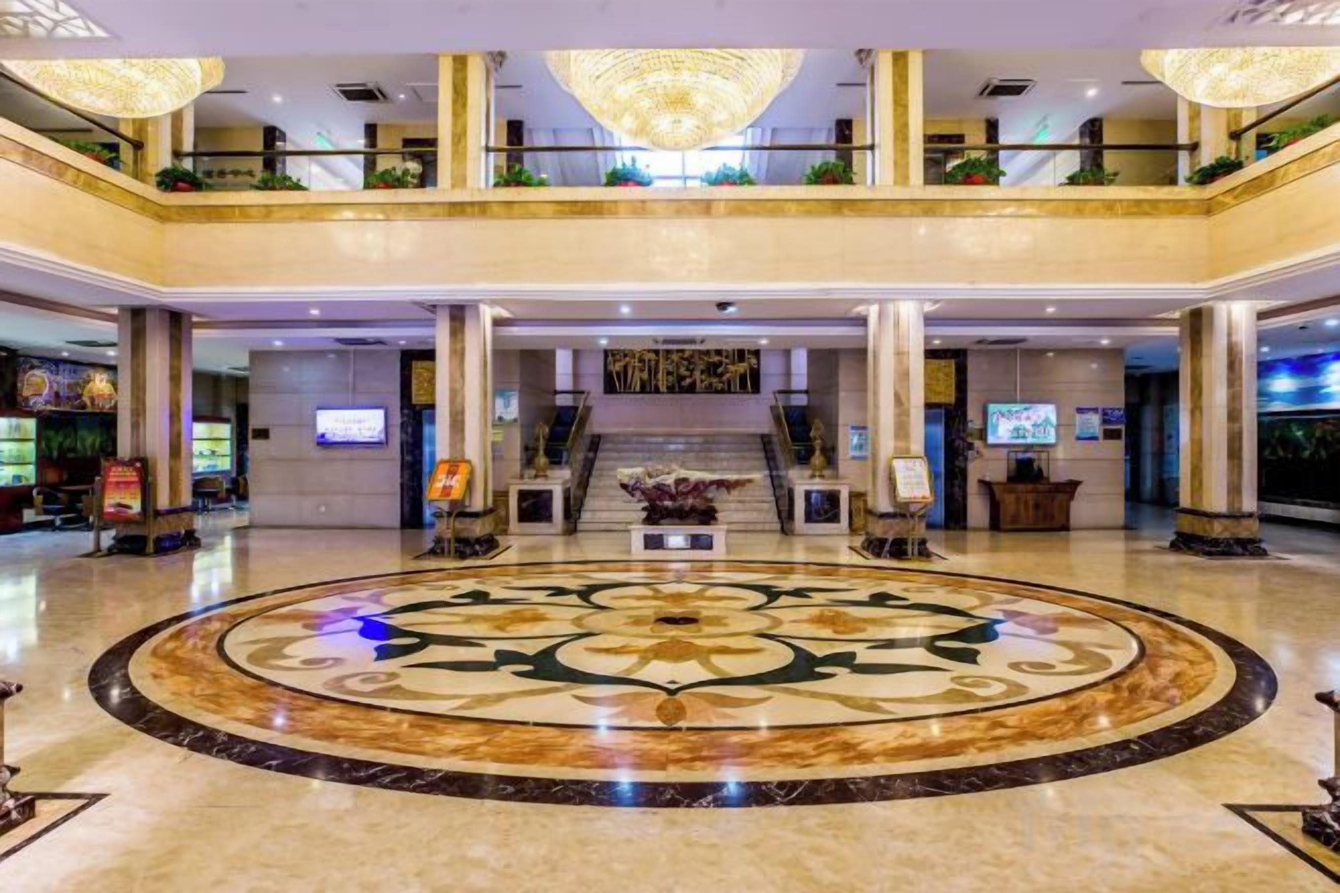 Un hall de hotel con un amplio piso circular de mármol, una recepción y una escalera que conduce a los niveles superiores.