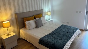 A neatly made bed with a grey headboard, two bedside lamps, and a striped wallpaper pattern on the wall. - Modern apartment 5 km from Carvoeiro with terrace and barbecue (Lagoa)