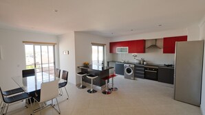 A modern kitchen with a central island, a dining area with a glass table and chairs, and a washing machine. - Modern apartment 5 km from Carvoeiro with terrace and barbecue (Lagoa)