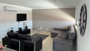 A modern living room with a flat-screen TV, a sofa, a coffee table, and a decorative clock on the wall. - Modern apartment 5 km from Carvoeiro with terrace and barbecue (Lagoa)