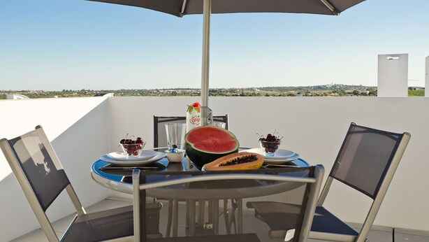 A table with a large umbrella, two chairs, and a plate with fruit and a drink. - Modern apartment 5 km from Carvoeiro with terrace and barbecue (Lagoa)