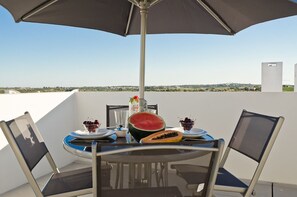 Ein Tisch mit einem großen Sonnenschirm, zwei Stühlen und einer Platte mit Obst und einem Getränk.