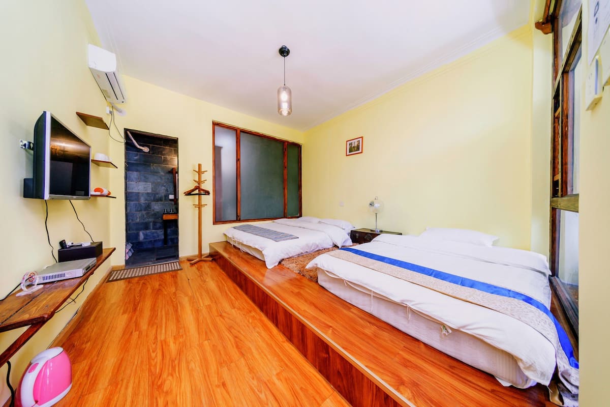 A room with two beds, a TV, a desk with a computer, and a shoe rack.