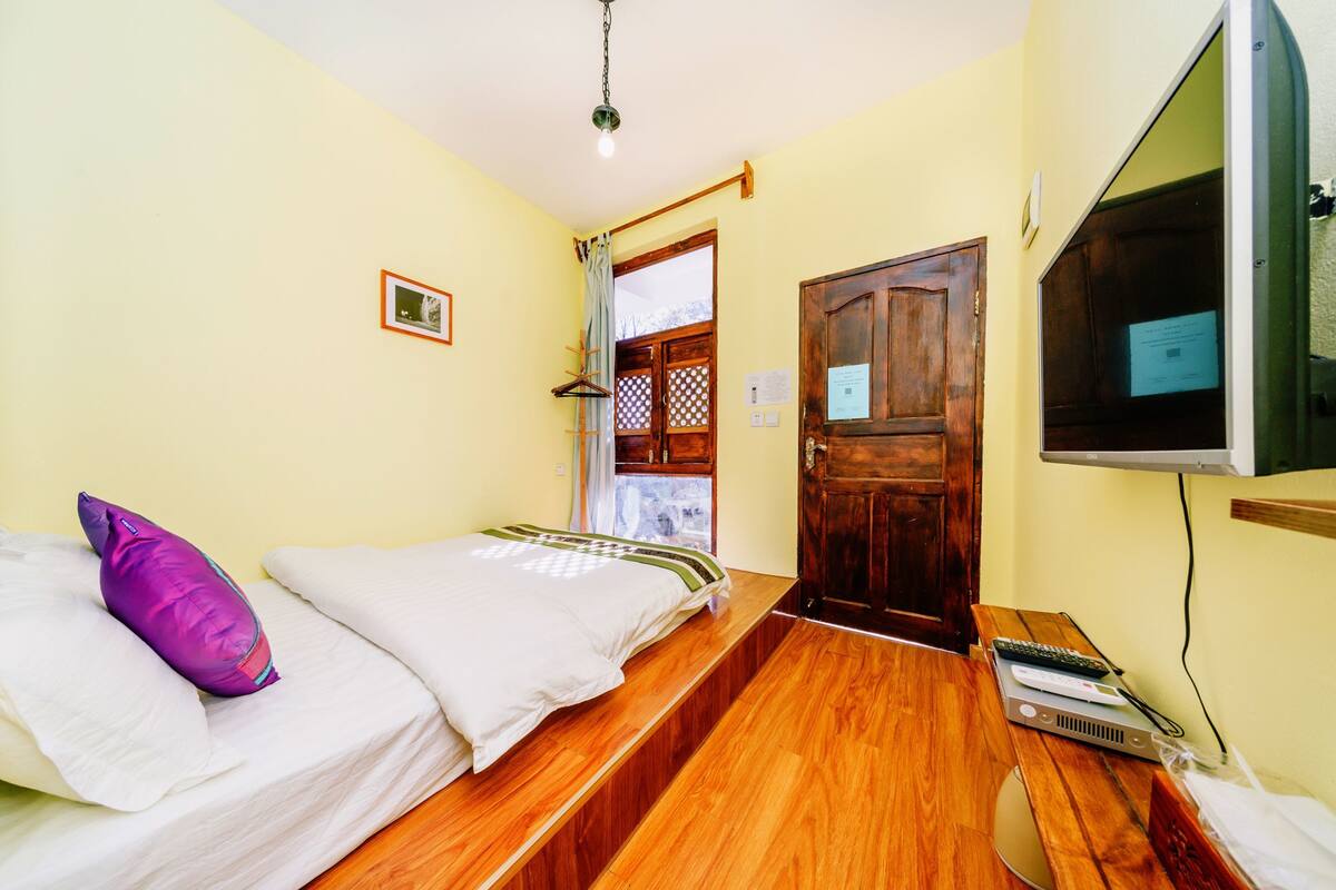 A bedroom with a bed, a wooden bench, a TV, and a door.