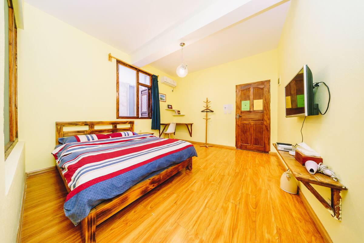 A bedroom with a wooden bed, a desk, a chair, a television, and a door.