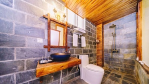 Un baño con pared de piedra, tocador de madera, inodoro blanco y zona de ducha.
