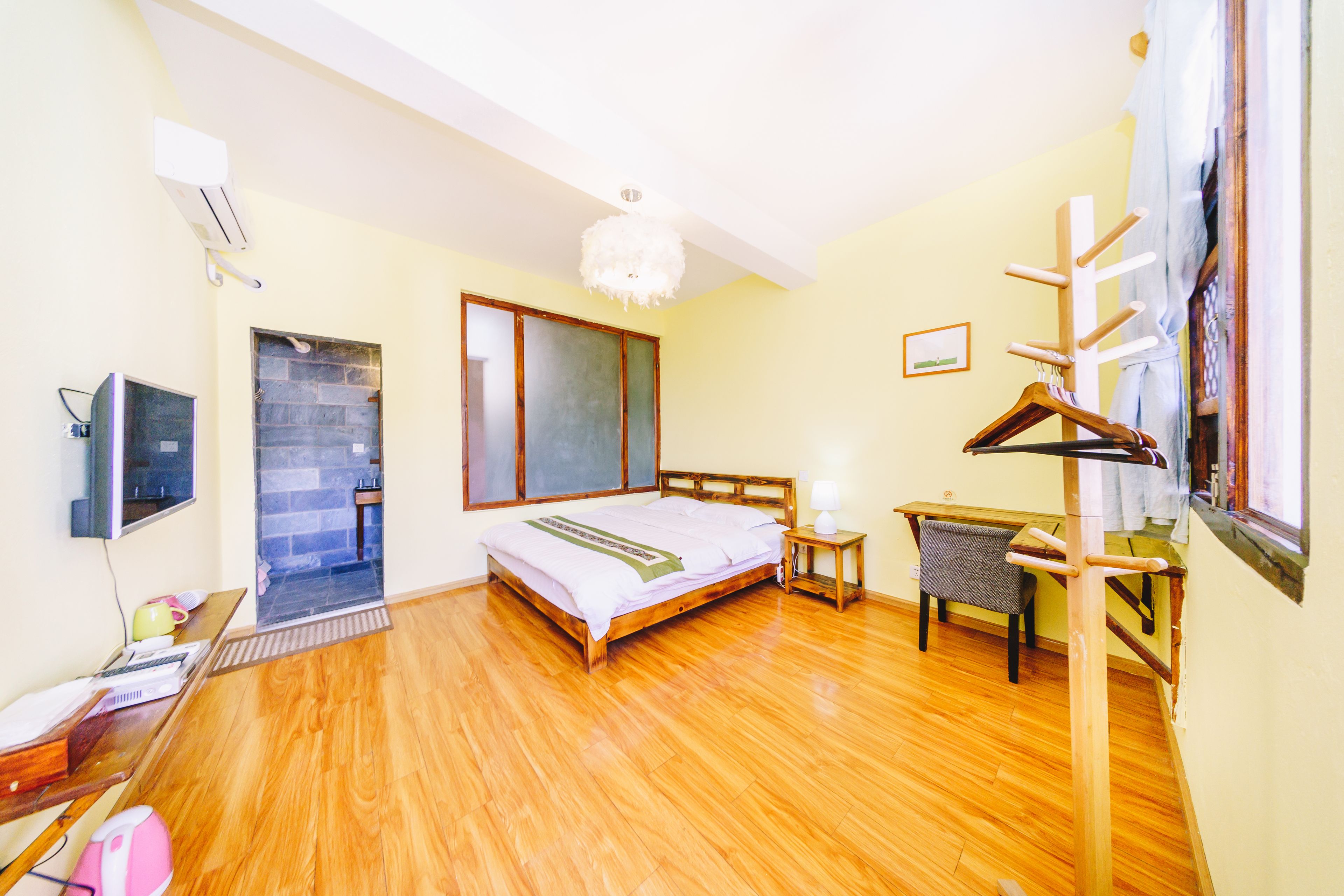 A bedroom with a wooden bed, a desk, a chair, a TV, and a wardrobe.