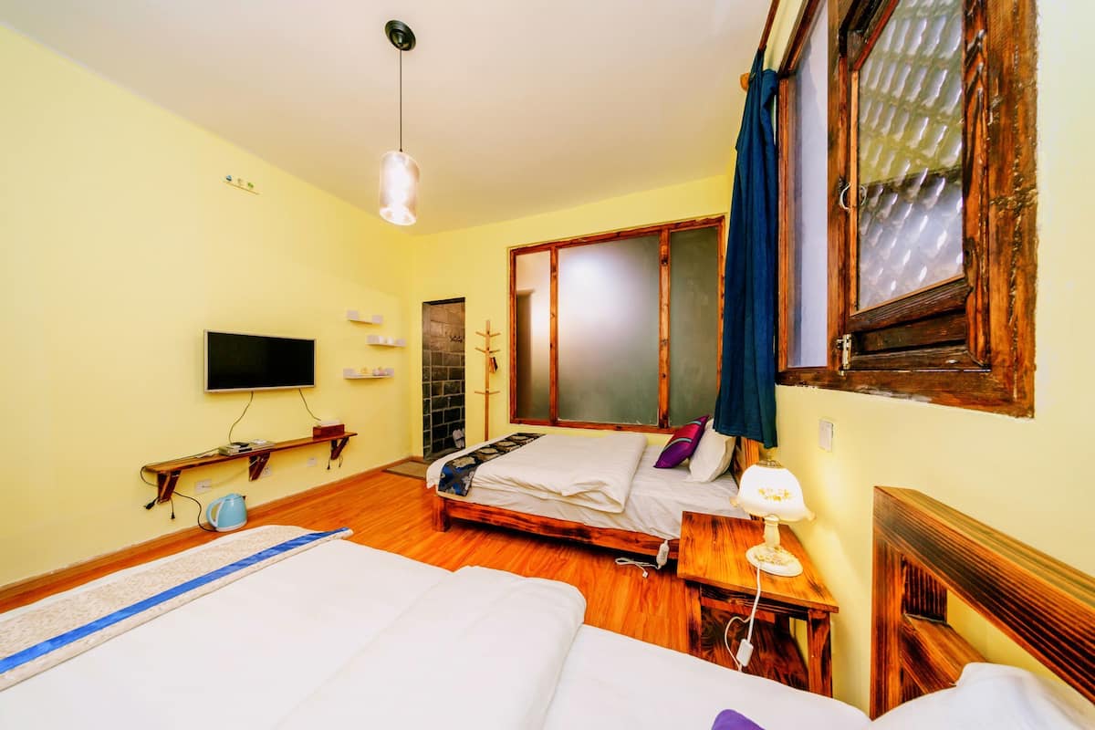 A hotel room with two beds, a TV, a wooden desk, and a window with curtains.