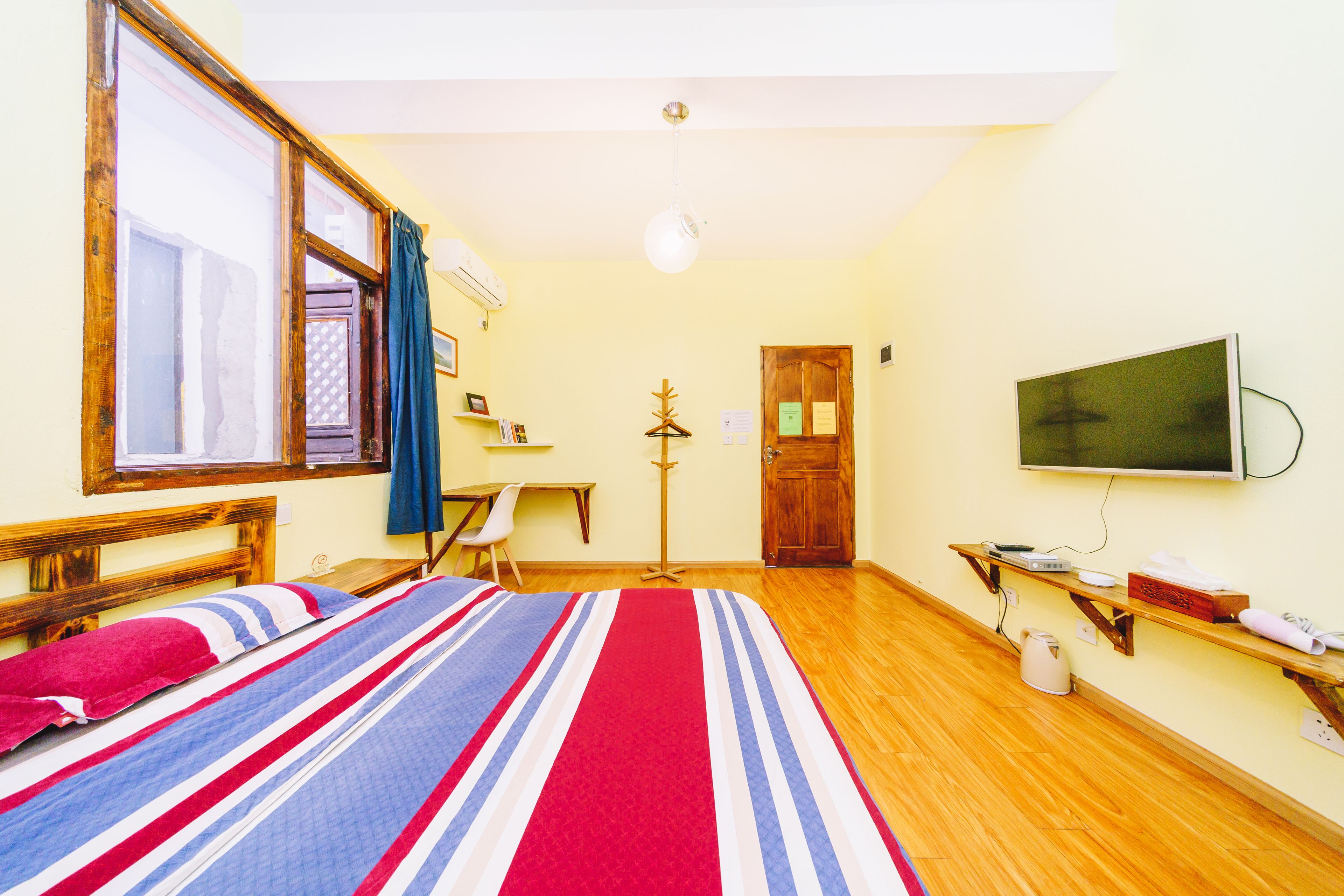 A room with a bed, a desk, a chair, a television, and a wooden floor.