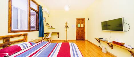 A room with a bed, a desk, a chair, a television, and a wooden floor.