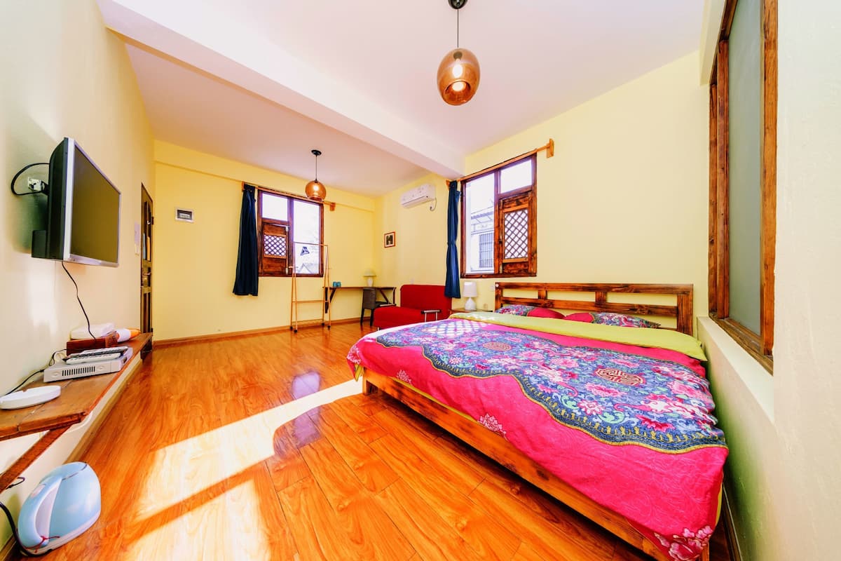 A bedroom with a large bed, wooden floor, a television, and a desk with a computer and other items.