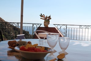 A table with a bowl of fruit, a glass, and a cup, set on a balcony overlooking a coastal view. - Spectacular view (Taormina)
