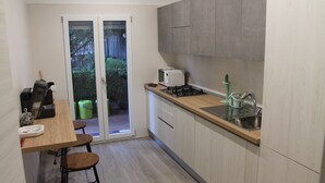 A compact kitchen with a wooden countertop, a sink, and a stove. There are two stools and a small table.