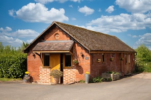 A brick building with a pitched roof, a wooden door, and a small porch with potted plants. - Little Owls Barn, Preston Wynne, Herefordshire (Preston Wynne)