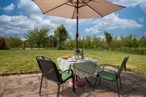 An outdoor patio with a table set for two, surrounded by chairs, under a large umbrella. - Little Owls Barn, Preston Wynne, Herefordshire (Preston Wynne)