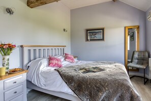A bedroom with a bed, pillows, a bedside table with a vase of flowers, a framed picture on the wall, and a chair. - Little Owls Barn, Preston Wynne, Herefordshire (Preston Wynne)