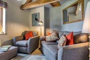 A living room with two grey sofas, one with a red pillow and the other with a floral pillow, a floor lamp, and a framed picture of a bird on the wall. - Little Owls Barn, Preston Wynne, Herefordshire (Preston Wynne)