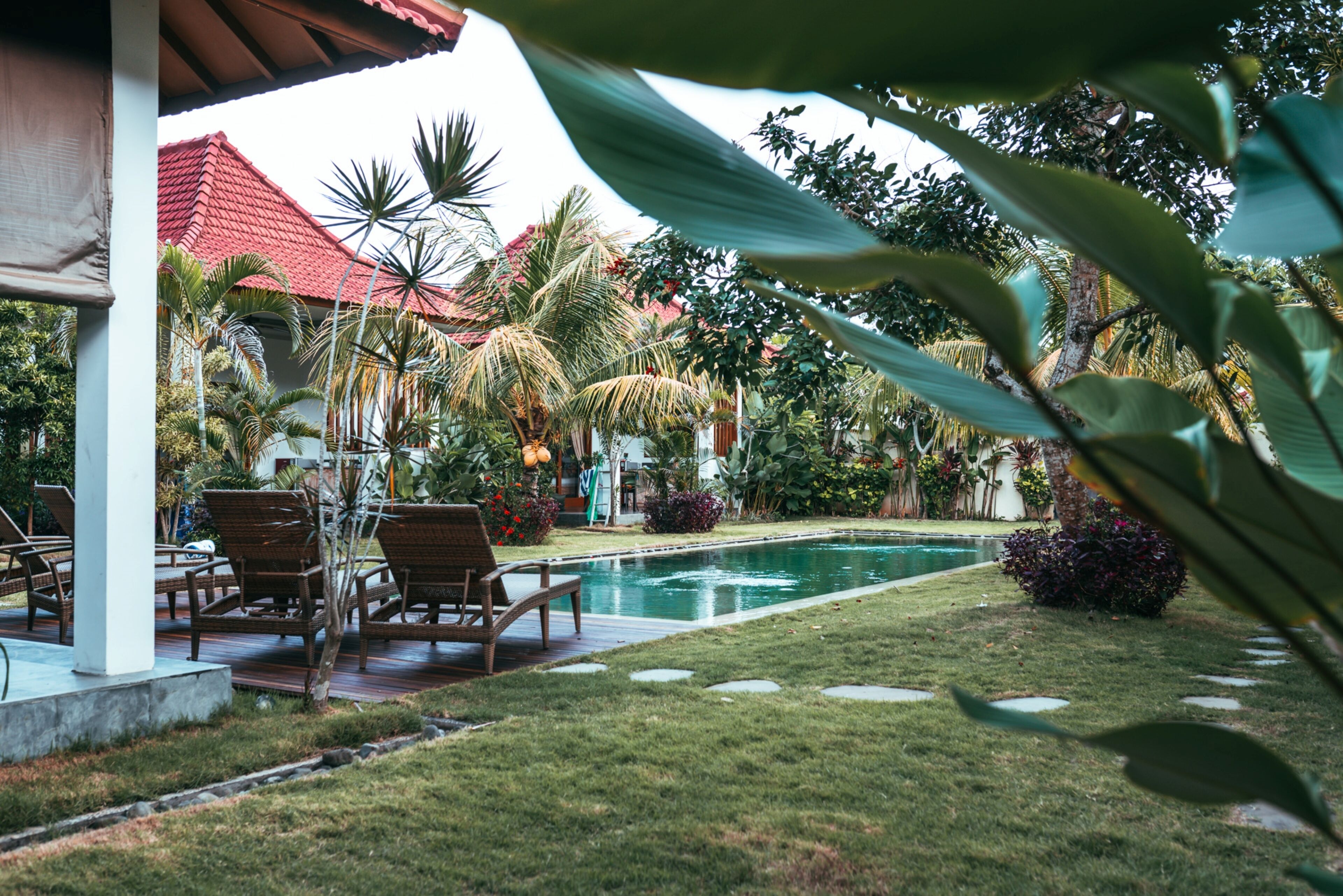 A pool area with lounge chairs, a red-roofed building, and tropical plants.